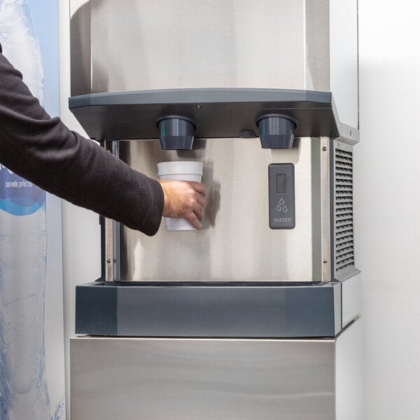 A person holding a cup of water in front of a Scotsman Meridian countertop ice and water dispenser.