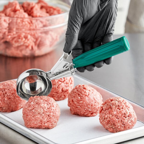 A person using a green-handled Green Thumb Press disher to scoop meatballs.