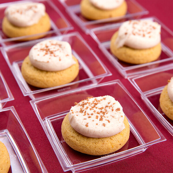 A group of WNA Comet Petites clear square dishes with small cookies with white frosting and sprinkles on top.