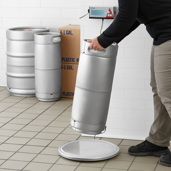 A person using a Taylor digital stainless steel keg scale to weigh a silver keg.