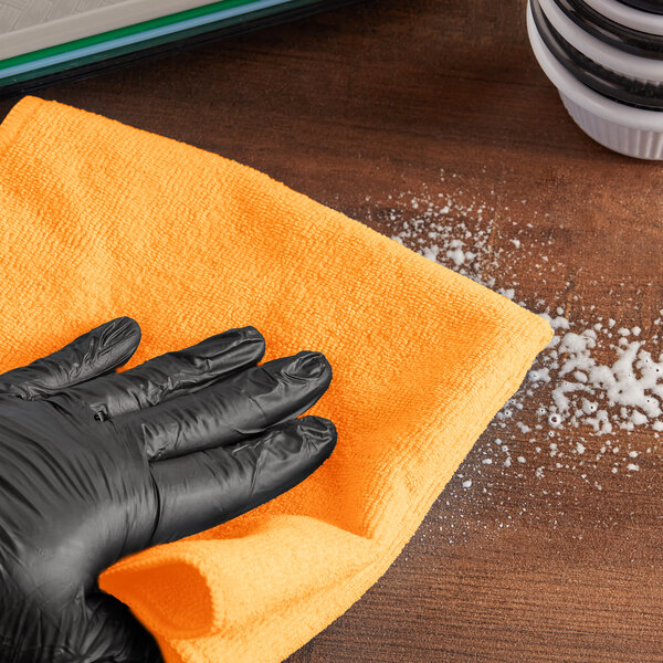 A person in a black glove cleaning a table with a yellow Lavex microfiber cloth.