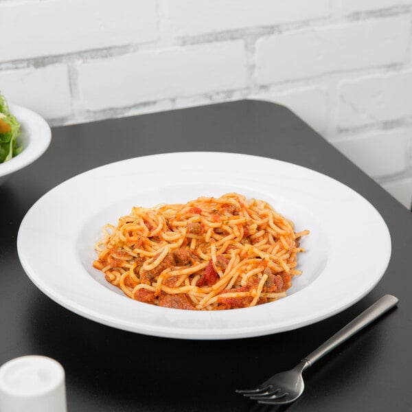 A white wide-rimmed bowl filled with salad next to a fork on a plate of spaghetti.