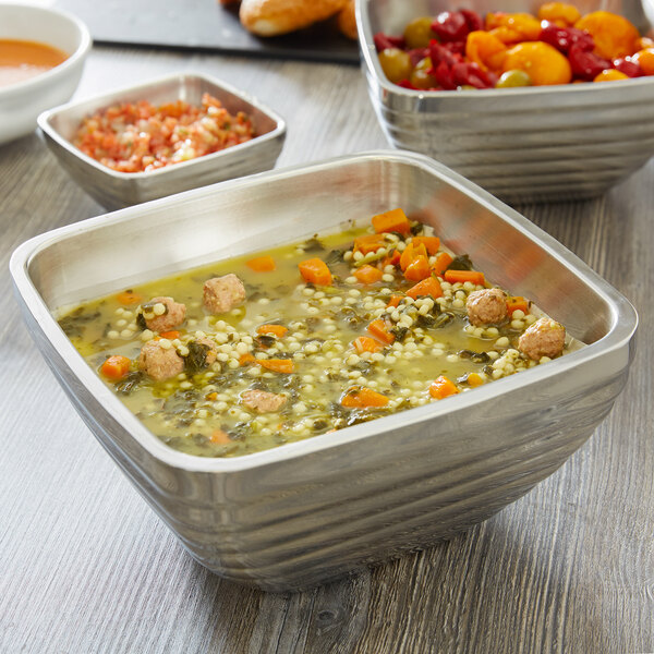 A Vollrath metal serving bowl with soup containing vegetables and meatballs.
