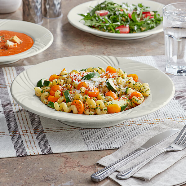 An Acopa Ivory stoneware pasta bowl filled with pasta and salad on a table.