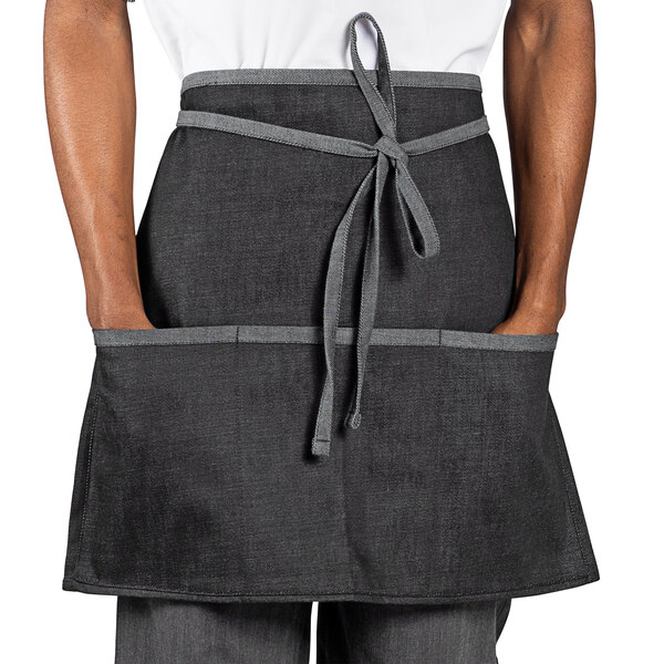 A man wearing a Uncommon Chef black denim waist apron with black webbing and pockets.