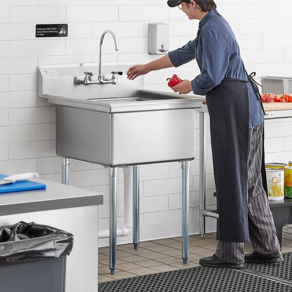 A woman in a blue apron standing at a Steelton 1 compartment sink.