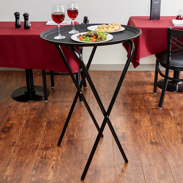A Lancaster Table & Seating black metal folding tray stand with food and wine glasses on it.