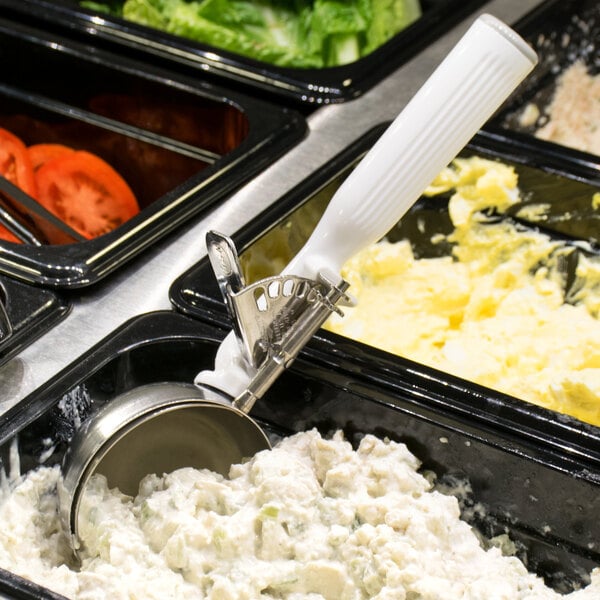 A tray of food with a Vollrath White Thumb Press Disher scooping food.