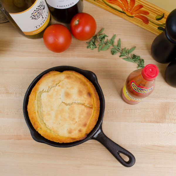 An American Metalcraft mini cast iron skillet with cornbread in it next to a bottle of sauce.