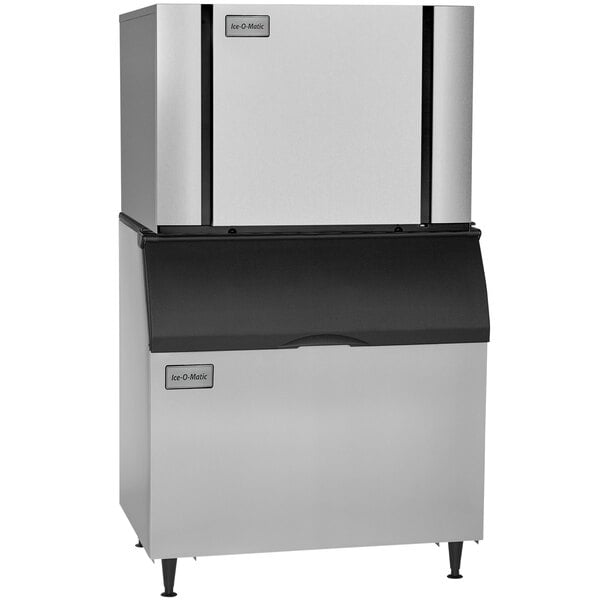 A stainless steel and black Ice-O-Matic ice machine with two trays inside.