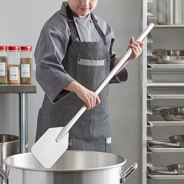A woman in a chef's uniform using an American Metalcraft stainless steel paddle in a kitchen.