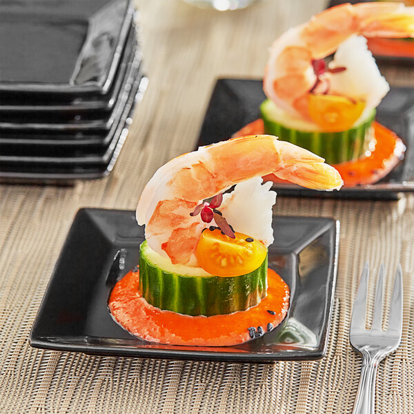 A glossy black Acopa stoneware plate with shrimp and cucumber on it.
