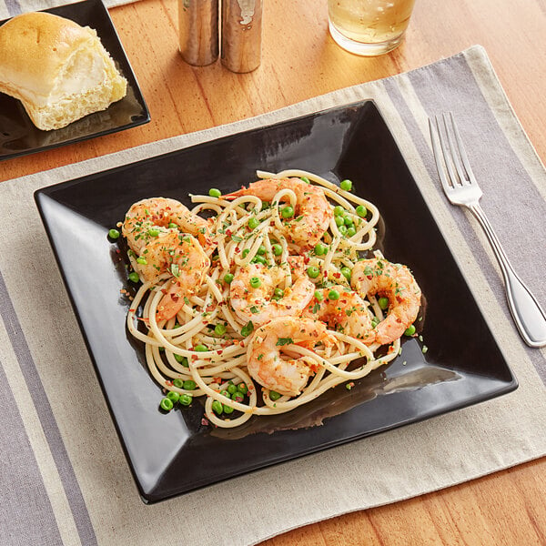A glossy black Acopa stoneware plate with spaghetti, shrimp, and peas on it.