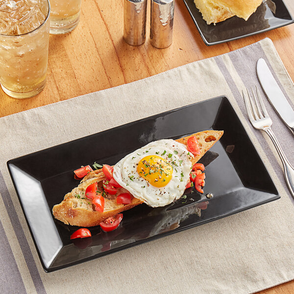 A rectangular black stoneware platter with a fried egg and a slice of bread on it.
