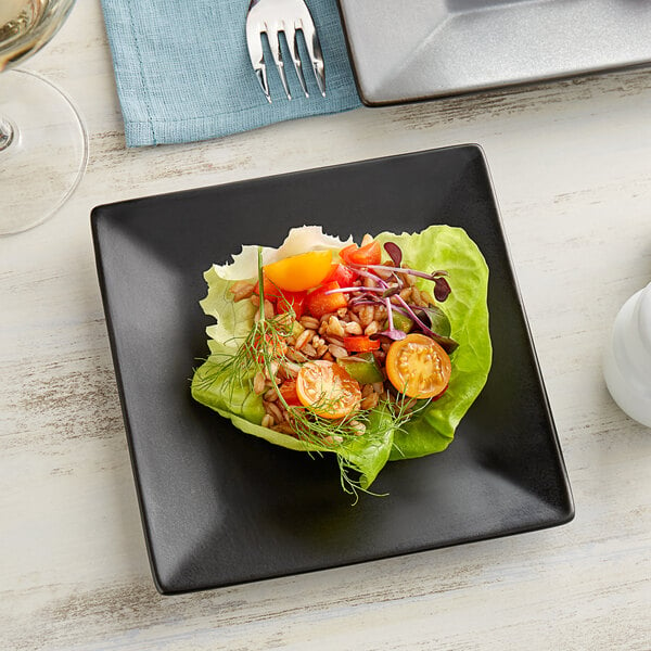 A plate of salad with lettuce, tomatoes, and other vegetables on a matte black square Acopa stoneware plate.