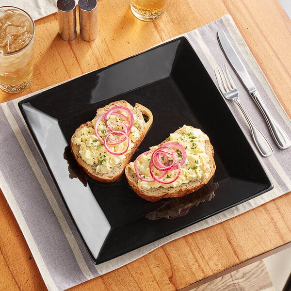 Two slices of toast on a glossy black Acopa stoneware plate with a fork and knife.