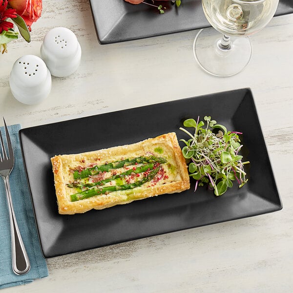 A rectangular matte black stoneware platter with a piece of asparagus and cheese pastry on it.
