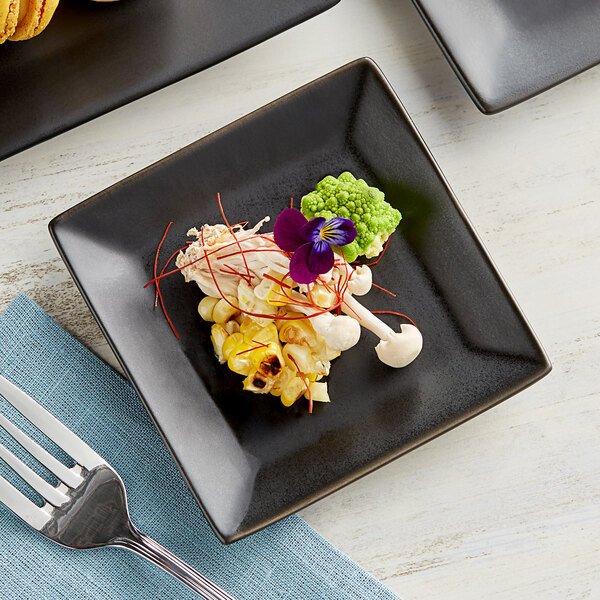 A Acopa matte black square stoneware plate with food and a fork on a table.