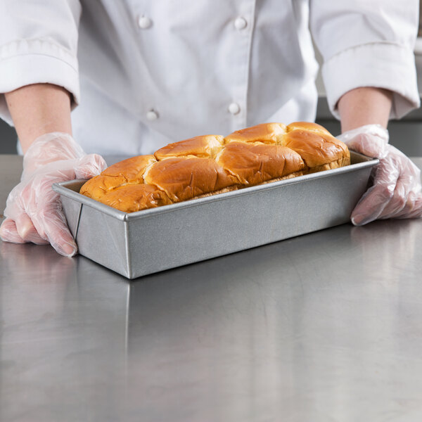 A person in gloves holding a loaf of bread in a Chicago Metallic bread loaf pan.