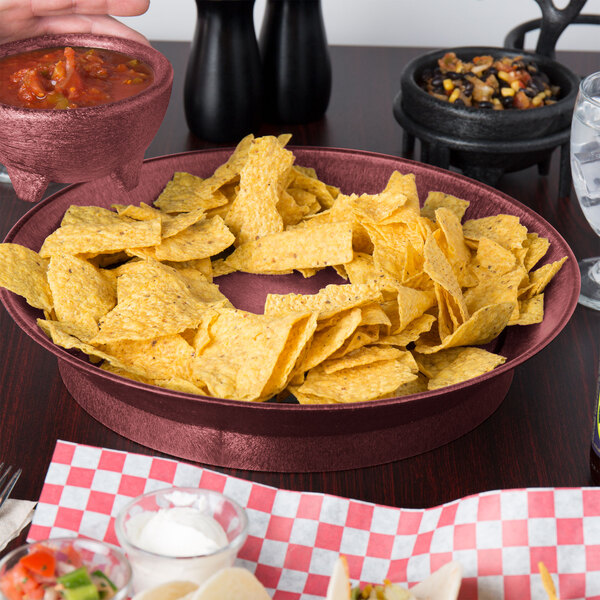 A HS Inc. round raspberry polypropylene deli server filled with tortilla chips on a table with a bowl of salsa.