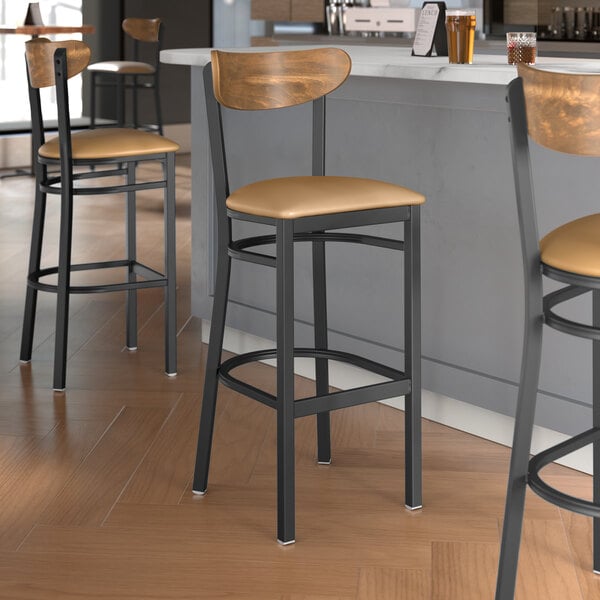 Lancaster Table & Seating Boomerang Series bar stools with light brown vinyl seats and vintage wood backs at a restaurant counter.