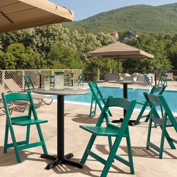 A Lancaster Table & Seating green folding chair on a table by a pool.