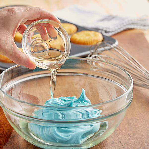 A person pouring LorAnn Preserve-It Antioxidant into blue frosting in a glass bowl.