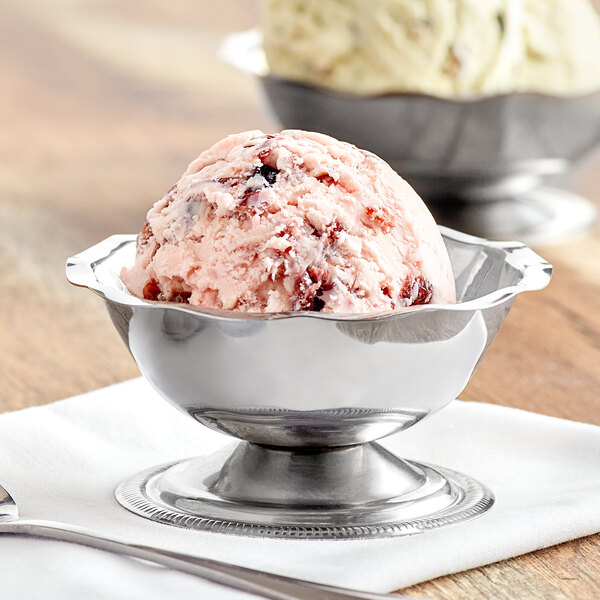 A stainless steel Vollrath round paneled sherbet dish filled with ice cream on a table.