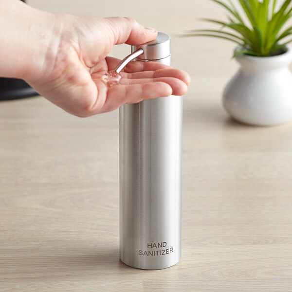 A person's hand holding a stainless steel hand sanitizer dispenser.
