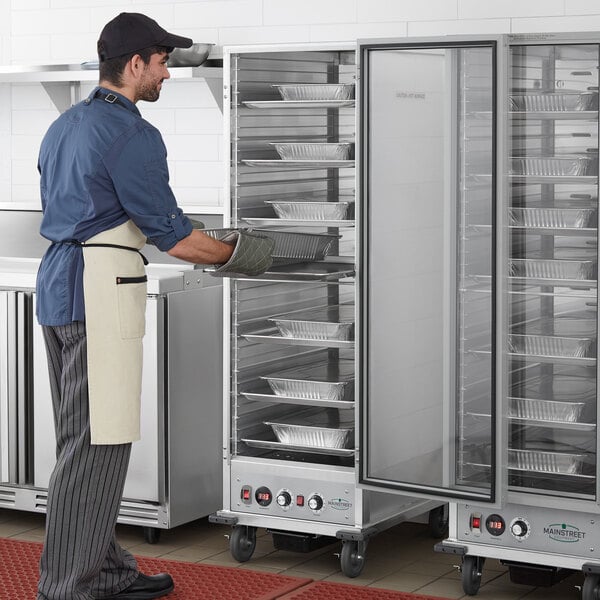 A man in a chef's uniform opening a Main Street Equipment heated holding / proofing cabinet with clear door.