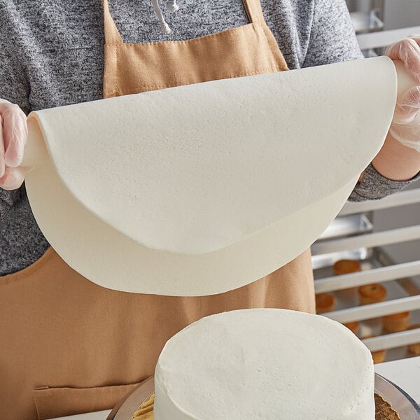 A woman using Satin Ice Dream white chocolate-flavored rolled fondant to cover a cake.
