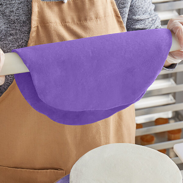 A person rolling purple Satin Ice fondant on a white surface.