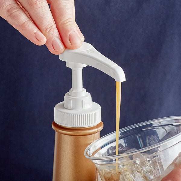 A person using a Tablecraft Flavoring Syrup Pump to pour liquid into a glass on a counter.
