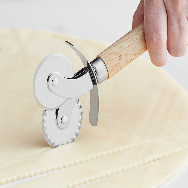 A hand using a Fox Run stainless steel double pastry cutter with wood handle to cut dough.