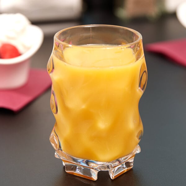 A GET SAN plastic dessert glass filled with orange juice on a table.