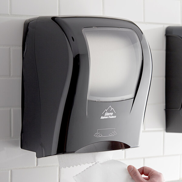 A person using a black Hygenics touch-free paper towel dispenser.