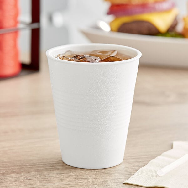 A Tablecraft white melamine tumbler filled with ice tea on a table.