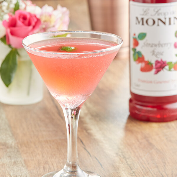 A glass of pink liquid made with Monin Premium Strawberry Rose flavoring syrup next to the bottle.