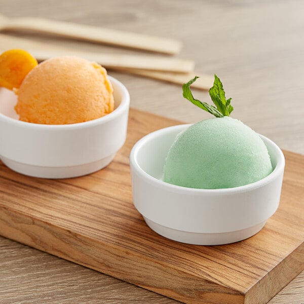 Two Tablecraft white mini melamine bowls with ice cream scoops of green and orange ice cream.