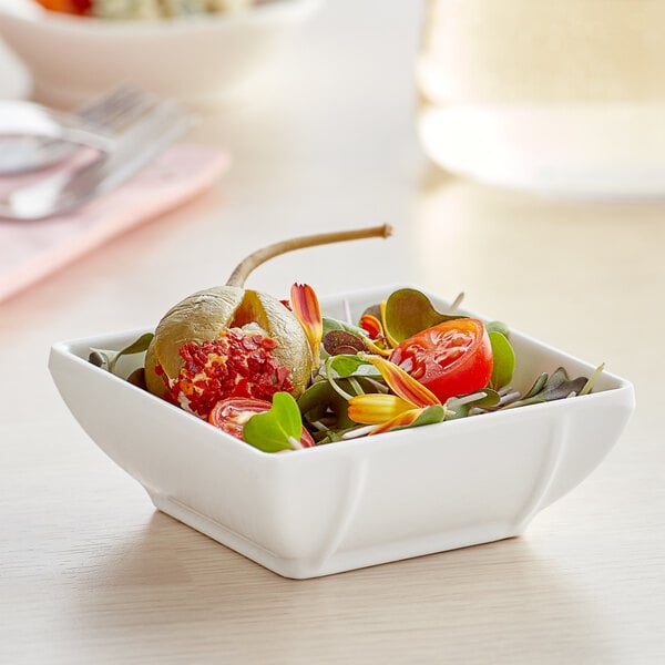 A Tablecraft square white melamine bowl filled with food on a table.