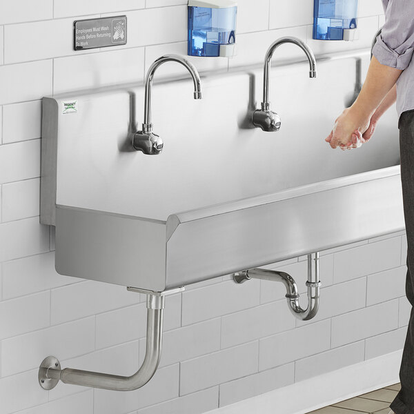 A man standing in front of a Regency stainless steel hand sink with 3 hands-free sensor faucets.