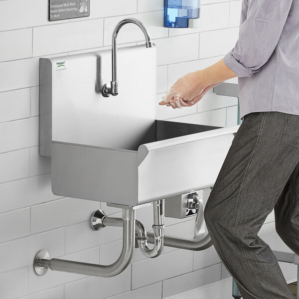 A person washing their hands in a Regency utility hand sink with knee operated faucet.