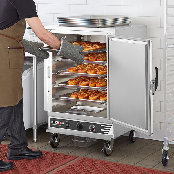 A man using a ServIt holding and proofing cabinet to put donuts on a tray.