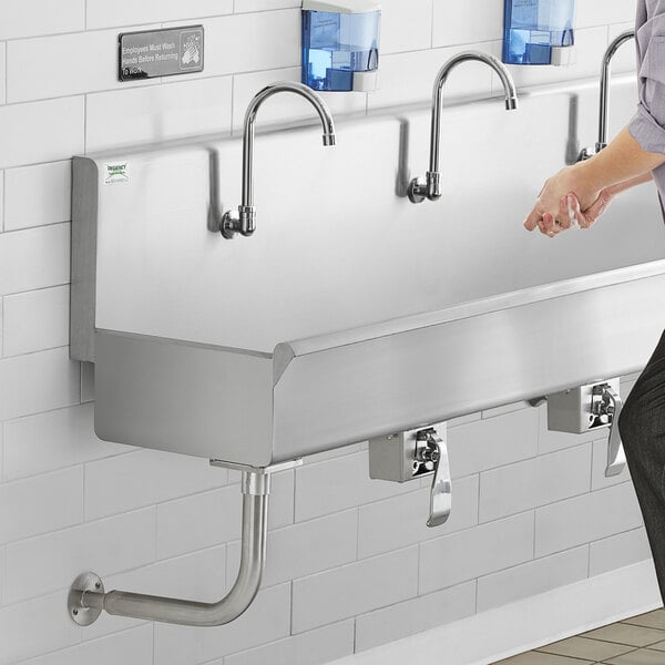 A person using a Regency multi-station hand sink with knee-operated faucets.