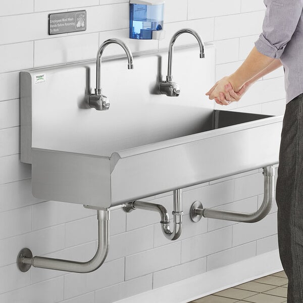 A man washing his hands in a stainless steel Regency multi-station hand sink.
