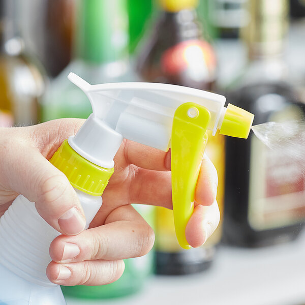 A hand holding a Lavex yellow plastic spray bottle trigger.