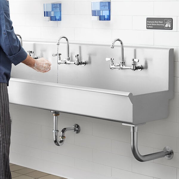 A person washing hands with soap under the Regency Multi-Station Hand Sink.