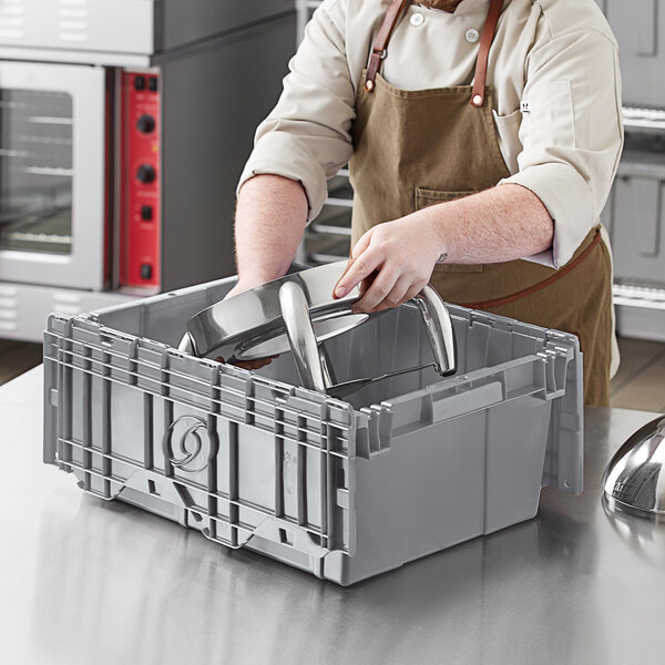 A man in an apron holding a metal object in a grey plastic box.