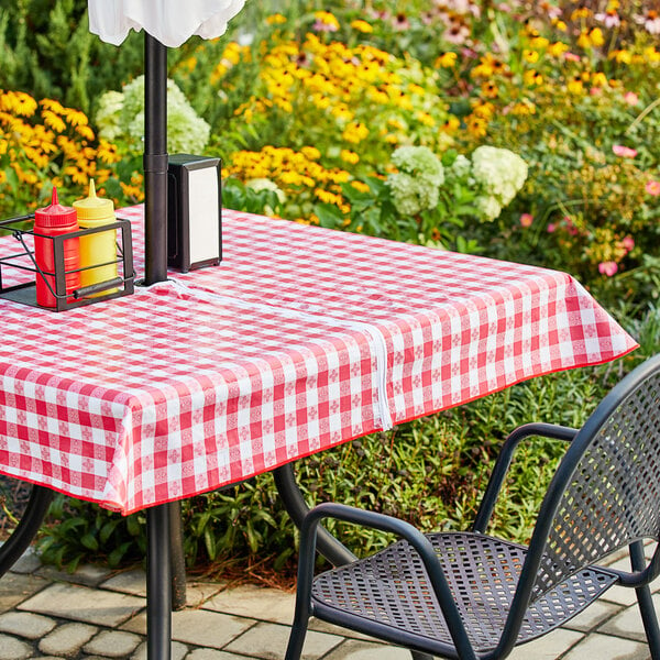 A table with a red and white checkered Choice vinyl table cover and umbrella opening over it.
