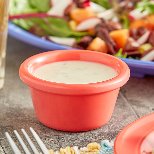 An orange smooth melamine ramekin filled with white sauce on a table.